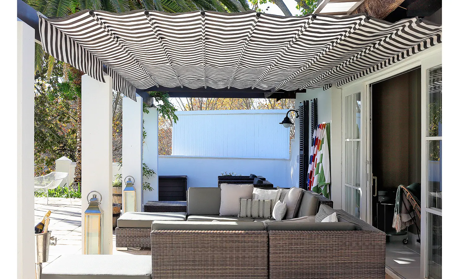 04| Perfect Hideaways: A cosy shaded terrace with cushioned rattan seating beneath a bold black-and-white striped awning invites relaxed outdoor lounging. Buitenzorg Pool Cottage, Constantia.