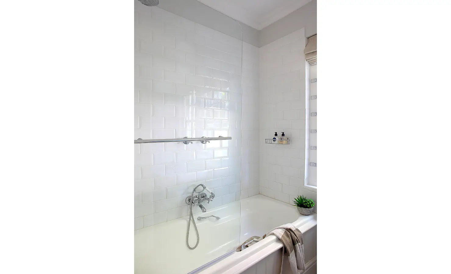 11| Perfect Hideaways: A bright white bathroom with subway tiles and chrome fixtures features a combined bath and shower beneath a tall window. Buitenzorg Pool Cottage, Constantia.