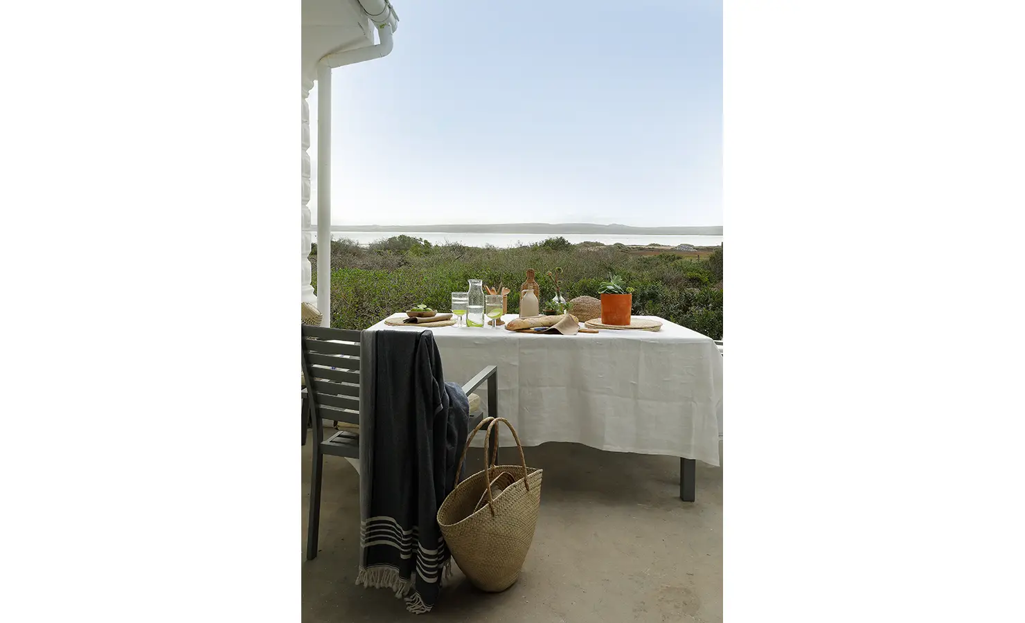 Perfect Hideaways: A serene outdoor dining table set with rustic crockery and natural decor, overlooking lush greenery and a calm coastline. Berit's Cottage, Churchhaven.