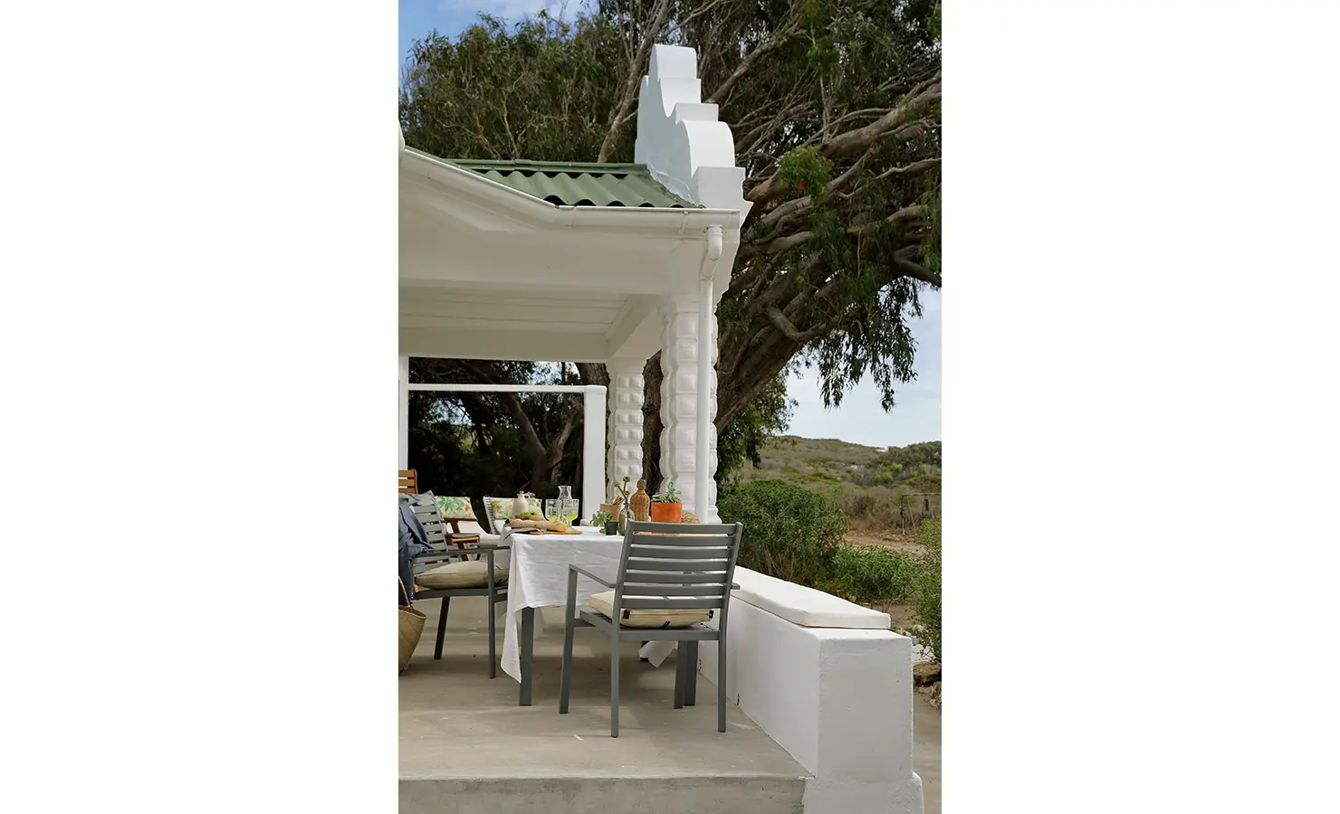 Perfect Hideaways: A charming veranda with a dining table under a green corrugated roof, surrounded by trees and natural vegetation. Berit's Cottage, Churchhaven.