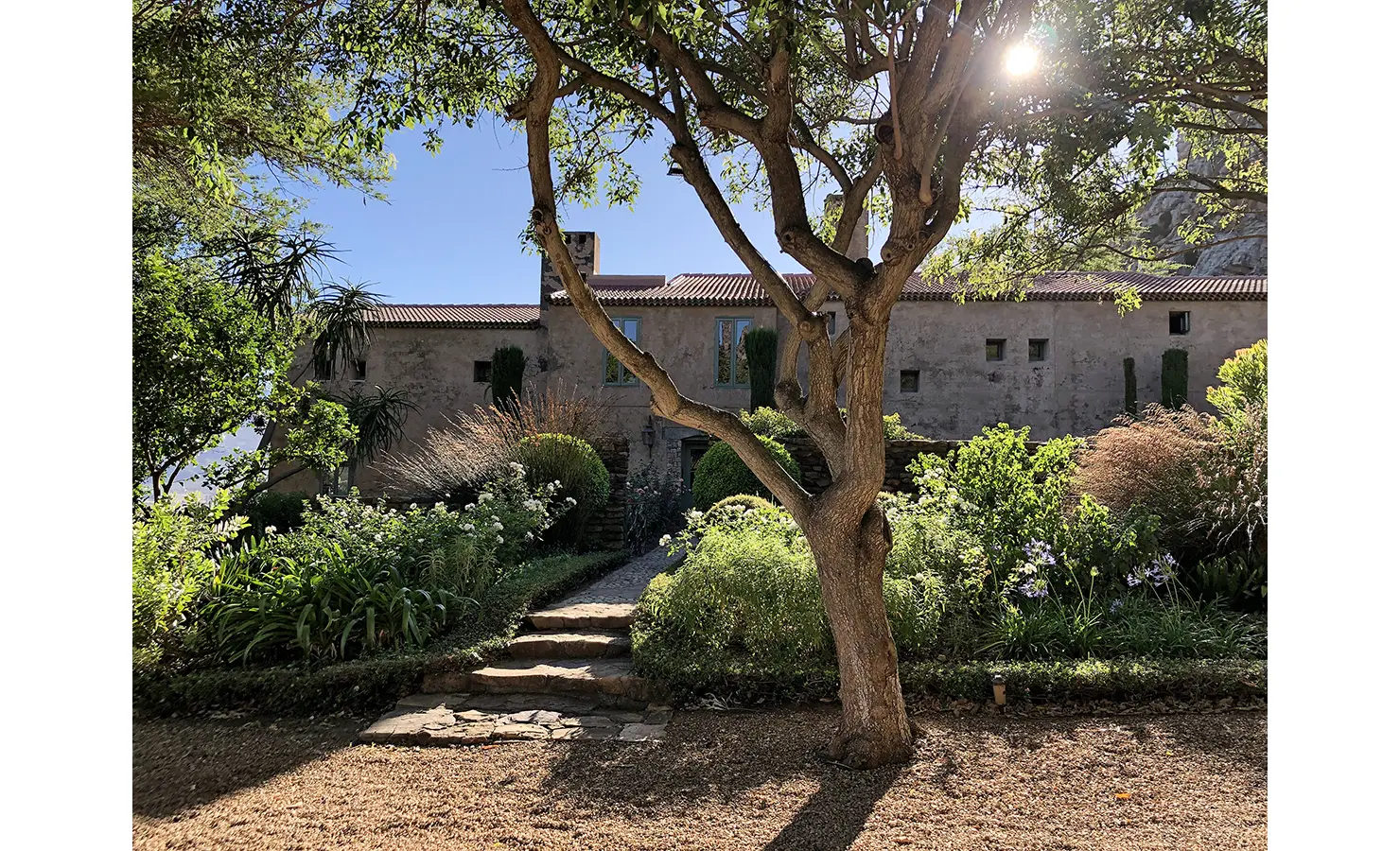 Perfect Hideaways: A picturesque Mediterranean-style manor surrounded by lush gardens, where dappled sunlight filters through the trees, creating a tranquil and enchanting atmosphere. Montpellier Manor House, Franschhoek.
