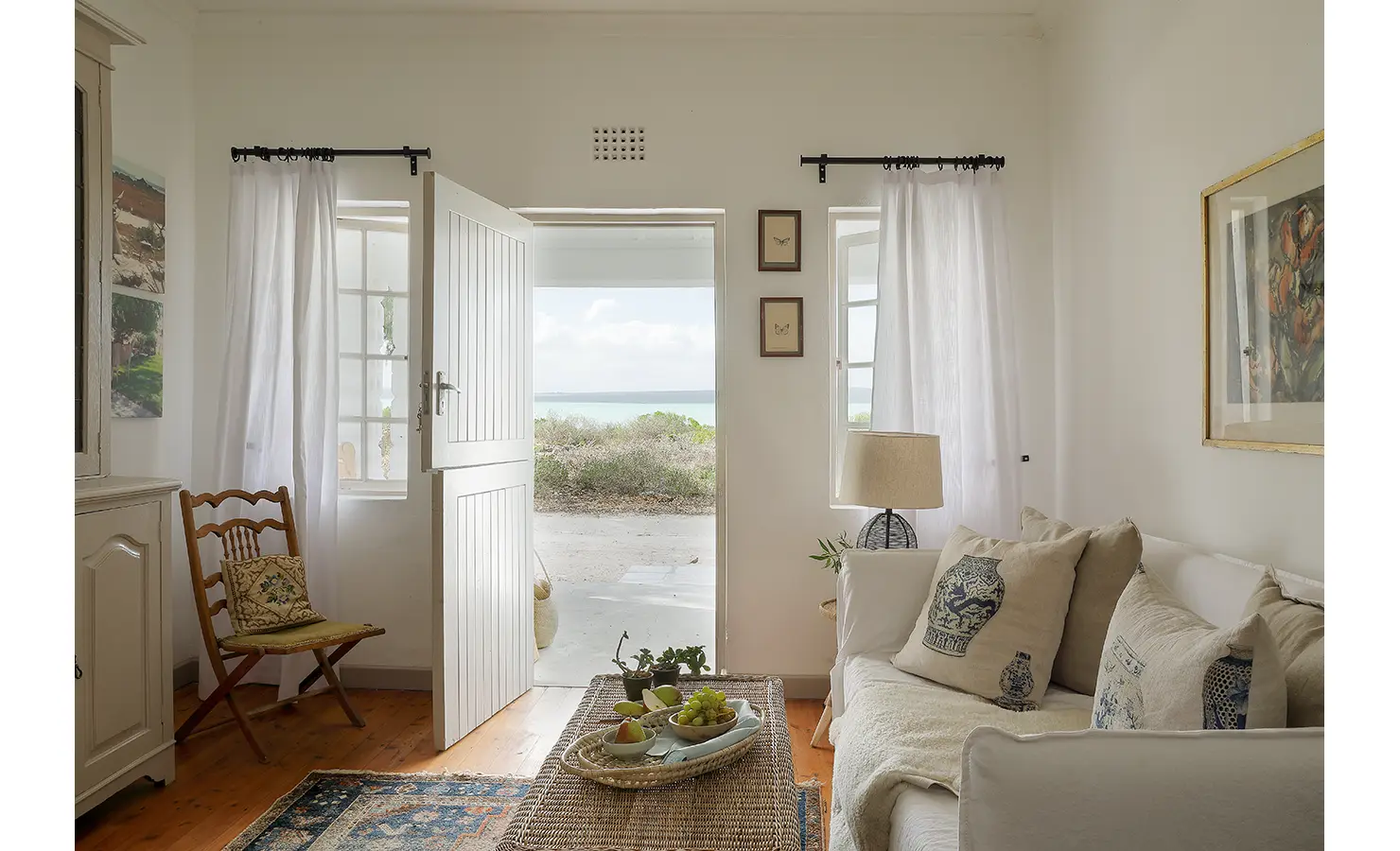 Perfect Hideaways: A cosy interior view of the living room with natural light streaming in through open double doors, revealing coastal greenery outside. Berit's Cottage, Churchhaven.