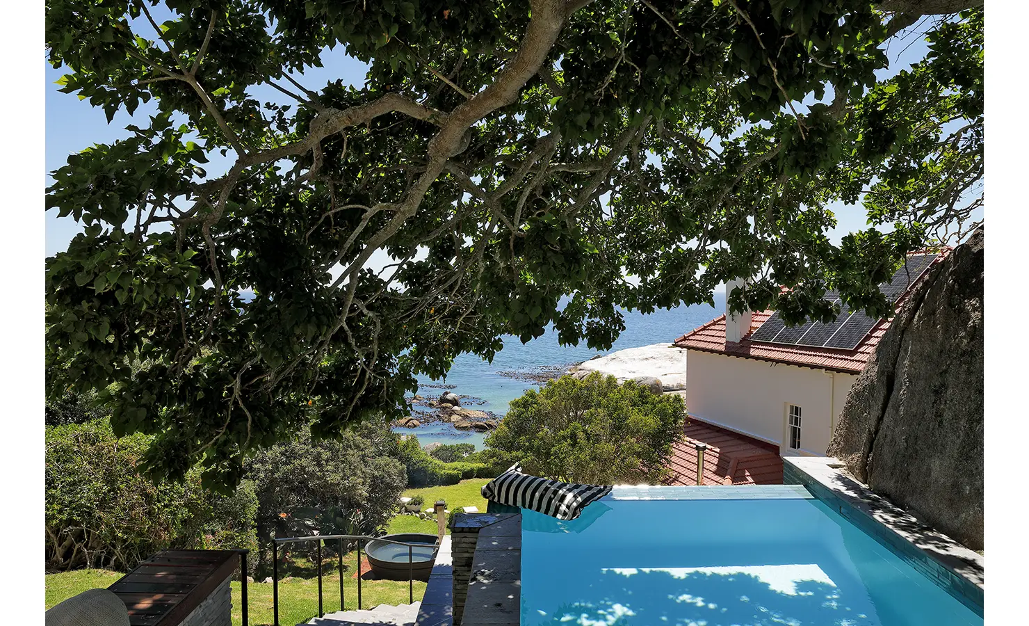 Perfect Hideaways: A private plunge pool nestled under a canopy of lush green foliage, overlooking the turquoise ocean and rugged coastline. A peaceful escape with uninterrupted views of the bay. Boulders House, Simons Town.