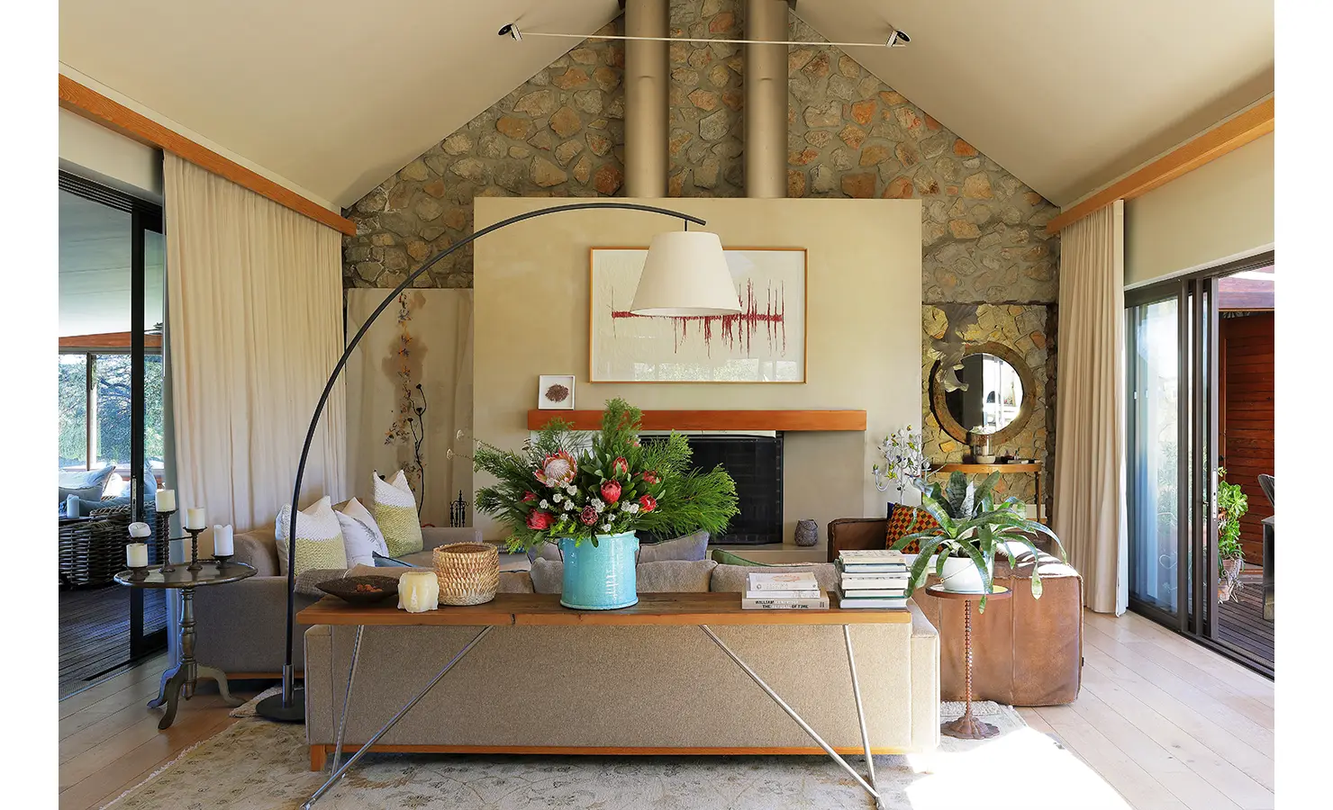 Perfect Hideaways: Elegant living room with stone feature wall, fireplace, large windows, and floral arrangement adding a touch of colour. Stonehaven House, Hemel-en-Aarde.
