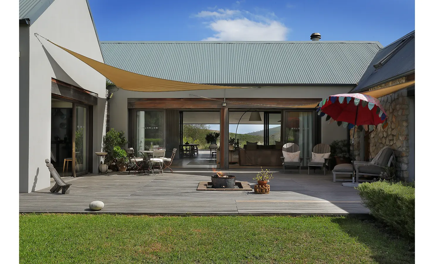 Perfect Hideaways: Sheltered outdoor terrace with canvas shade, eclectic seating, and a central firepit for evening gatherings. Stonehaven House, Hemel-en-Aarde.