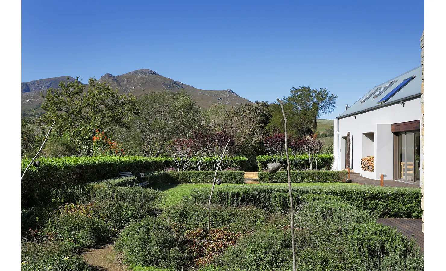 Perfect Hideaways: Formal garden framed by hedges, pathways, and mountain scenery under a bright blue sky. Stonehaven House, Hemel-en-Aarde.