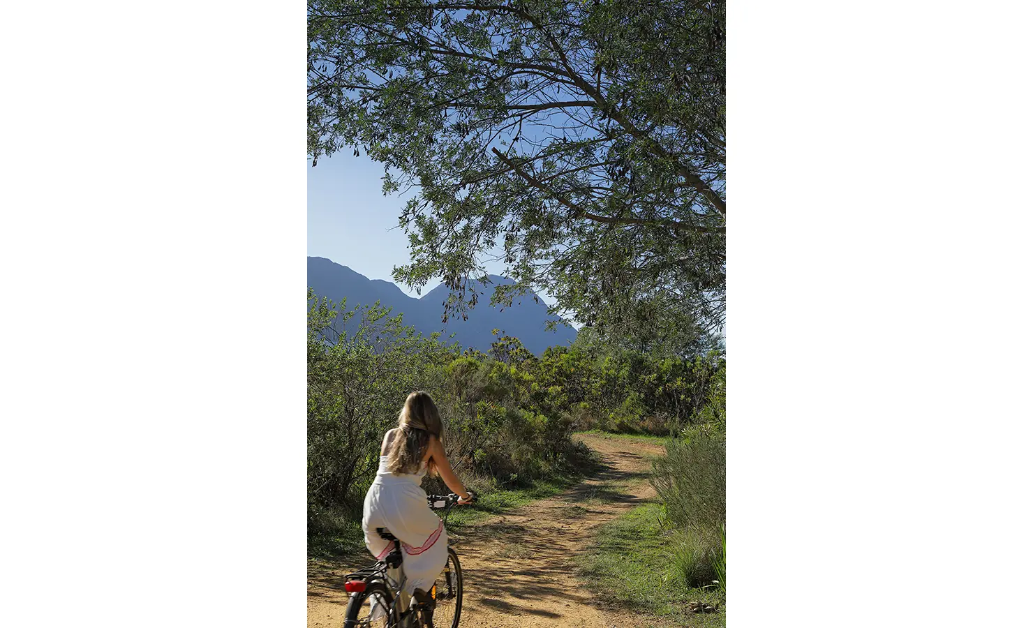 Perfect Hideaways: Guest cycling along a dirt path through natural fynbos with mountains in the distance. Stonehaven House, Hemel-en-Aarde.
