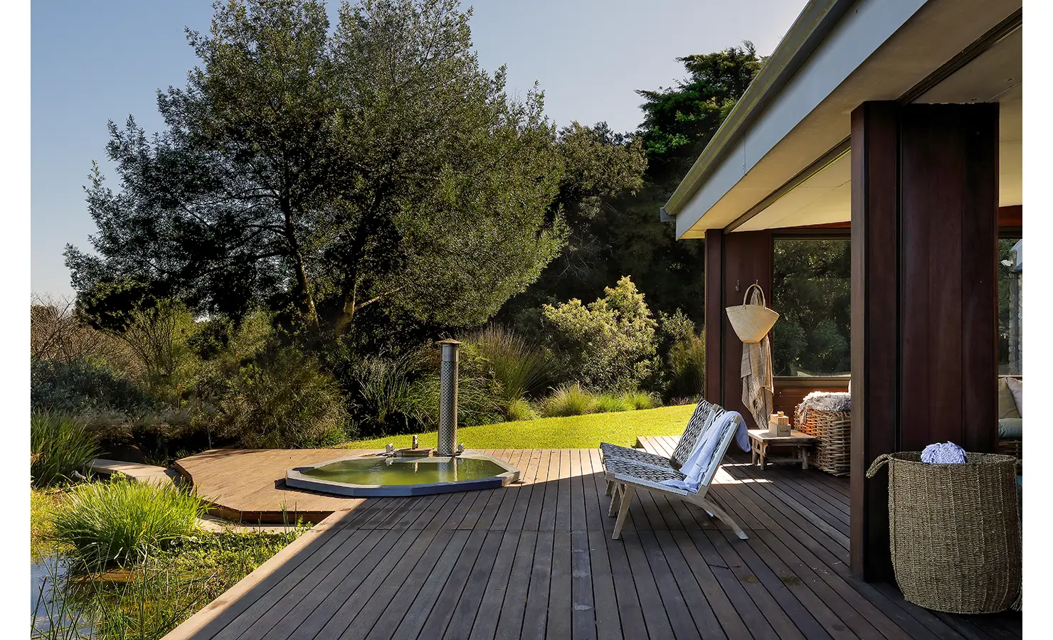 Perfect Hideaways: Timber deck with lounge chairs and views across lush greenery, leading to a wood-fired hot tub. Stonehaven House, Hemel-en-Aarde.