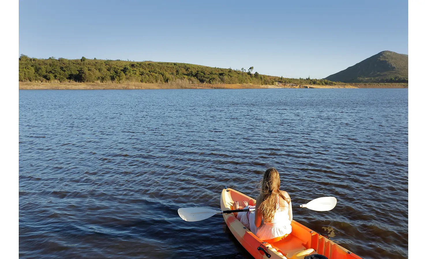 Perfect Hideaways: Guest kayaking across the tranquil dam, surrounded by rolling hills and mountain views. Stonehaven House, Hemel-en-Aarde.