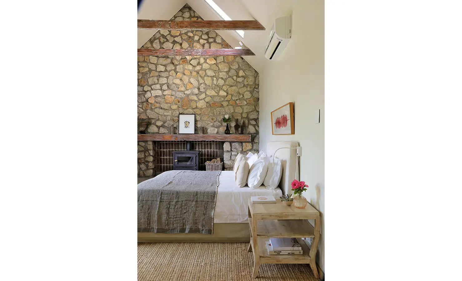 Perfect Hideaways: Bedroom with stone feature wall, exposed beams, wood-burning fireplace, and neutral linens. Stonehaven House, Hemel-en-Aarde.