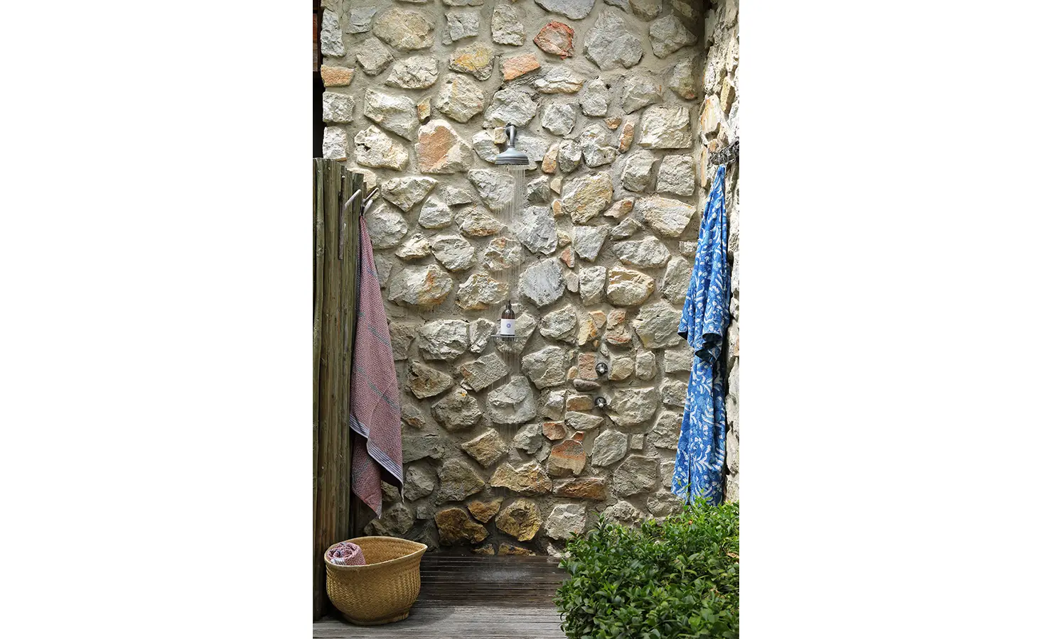 Perfect Hideaways: Outdoor shower set against a stone wall with colourful towels and a woven basket nearby. Stonehaven House, Hemel-en-Aarde.