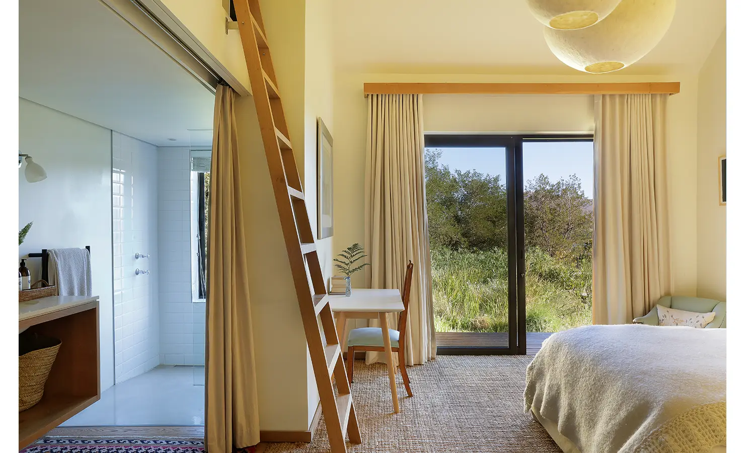 Perfect Hideaways: Light-filled bedroom with sliding doors to the garden, a small writing desk, and ladder leading to a loft. Stonehaven House, Hemel-en-Aarde.