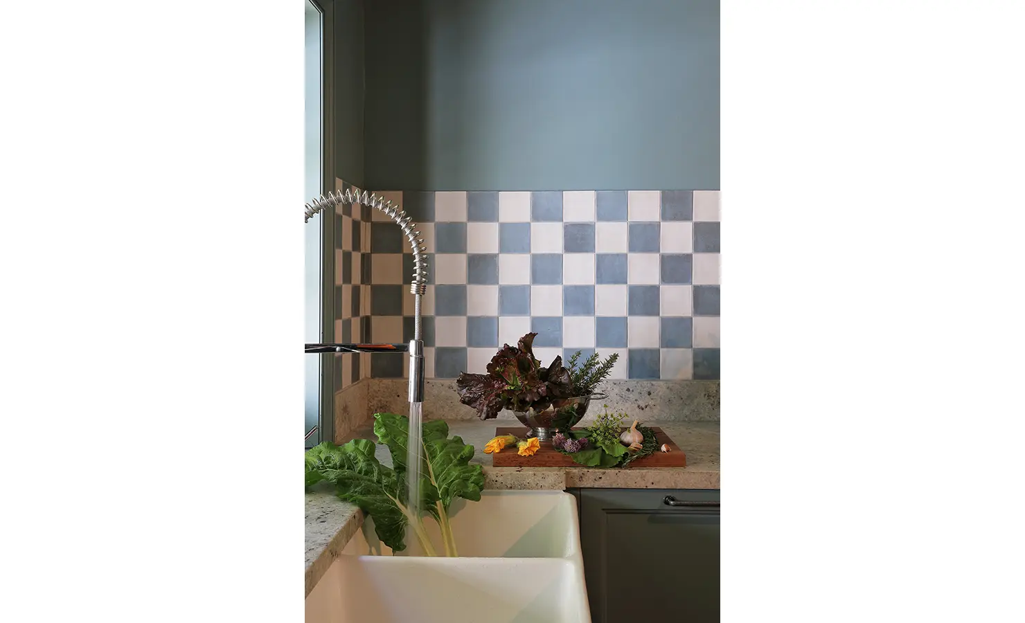 Perfect Hideaways — A cozy kitchen corner with a farmhouse sink and checkerboard blue-and-white tiled backsplash. Fresh vegetables and herbs rest beside the running water, evoking a rustic, homely charm. Bishopscourt, Bishops Hall.