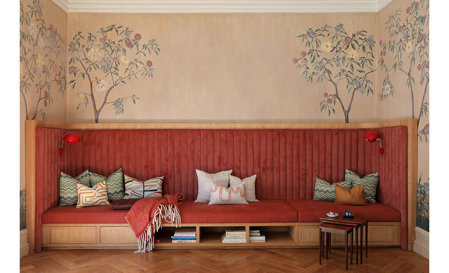 Perfect Hideaways — A corner lounge with a long red velvet built-in bench adorned with colorful patterned pillows and red reading lamps, set against hand-painted floral wall murals. Bishopscourt, Bishops Hall.