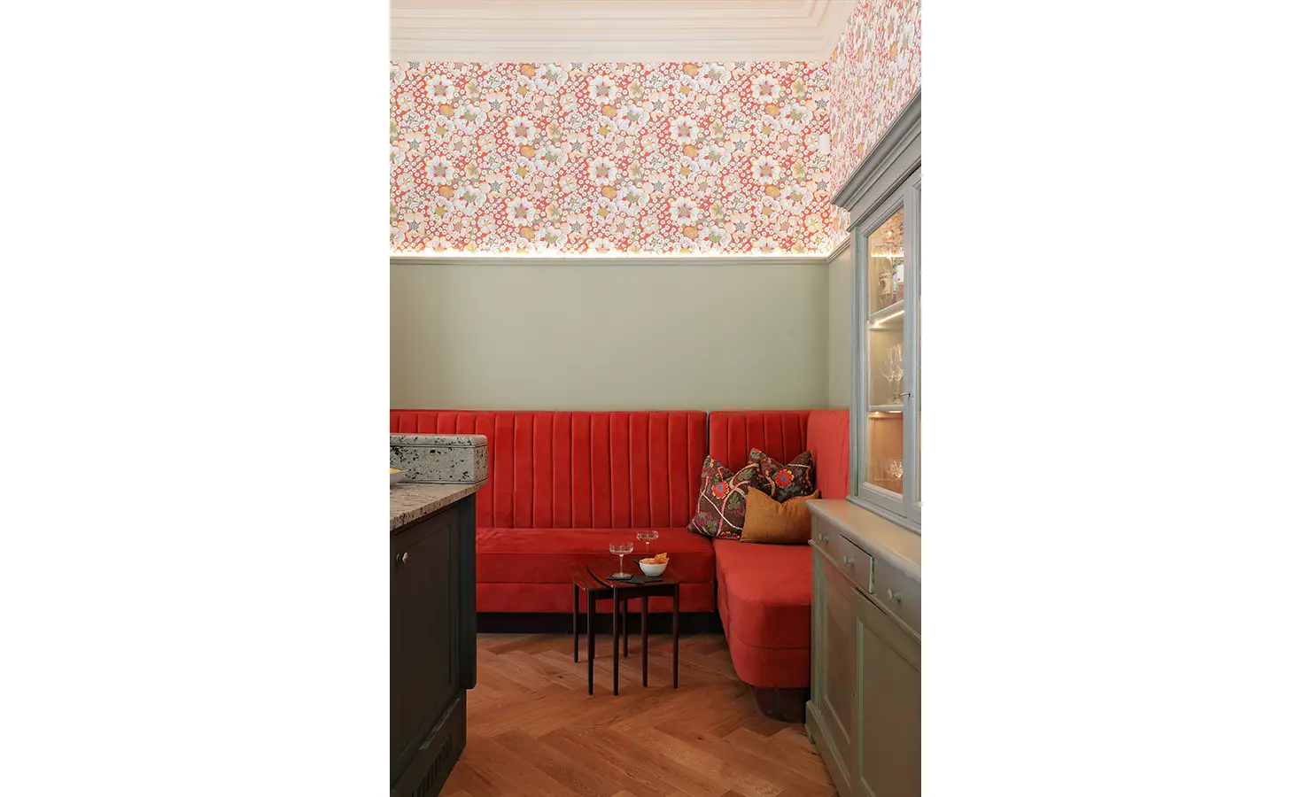 Perfect Hideaways — A close-up of the intimate bar nook with a coral-red banquette, floral wallpaper, and accent pillows. Two drinks rest on a small side table, perfect for a quiet evening in. Bishopscourt, Bishops Hall.