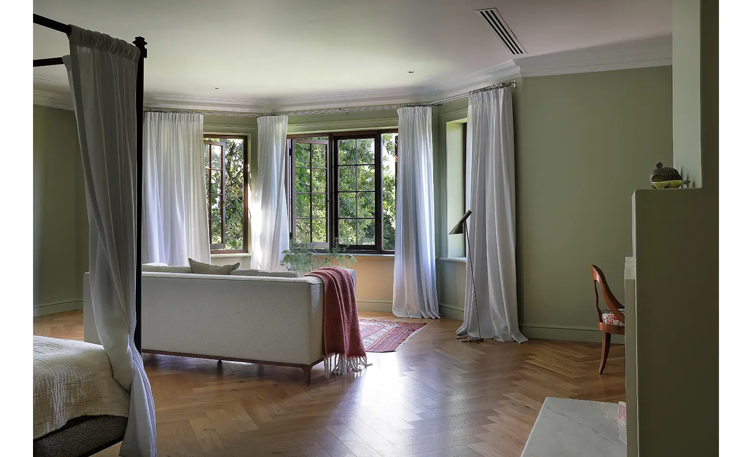 Perfect Hideaways — A serene bedroom seating area framed by large bay windows with flowing white curtains. Pale green walls, parquet flooring, and minimalist furniture invite peace and natural light. Bishopscourt, Bishops Hall.