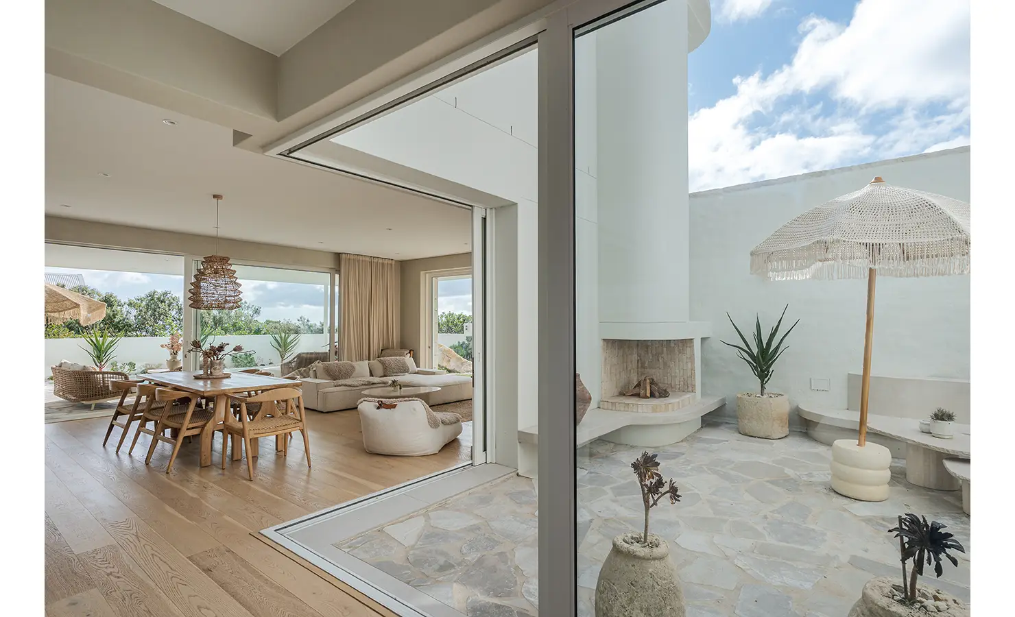 Perfect Hideaways: A seamless indoor-outdoor living space featuring a spacious dining area, a plush lounge, and a cosy courtyard with a built-in fireplace. Natural textures, soft furnishings, and earthy tones create a warm and inviting atmosphere. Seaside Sanctuary, Scarborough.