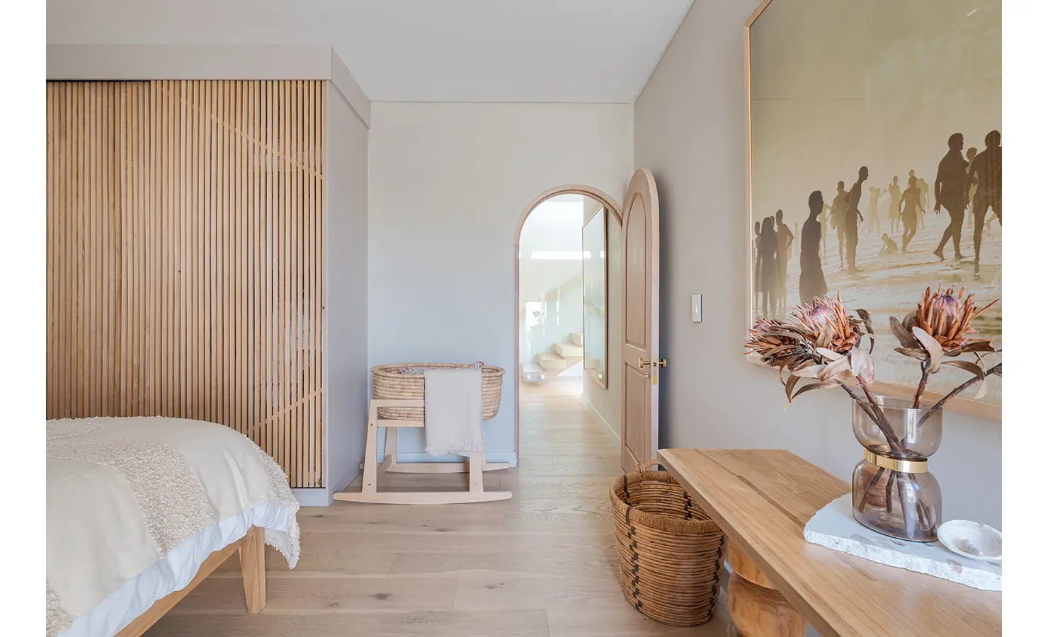 Perfect Hideaways: A beautifully designed bedroom with a wooden slatted wardrobe, an arched doorway, and warm natural textures. A vintage-style beach scene artwork and woven décor enhance the relaxed, coastal-inspired atmosphere. Seaside Sanctuary, Scarborough.