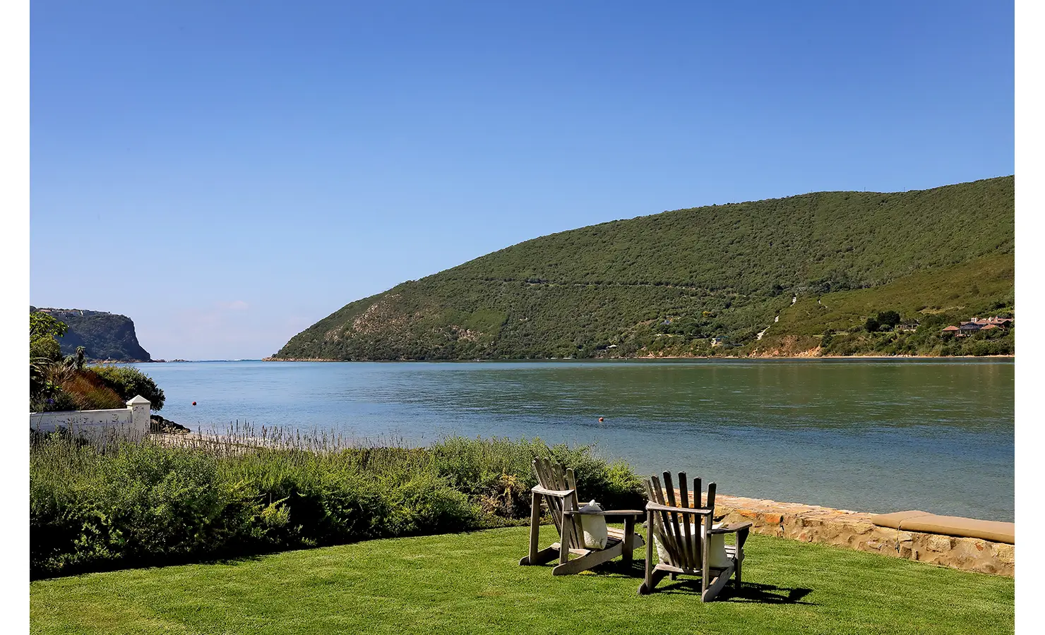 Perfect Hideaways: Adirondack chairs on a lawn facing the tranquil lagoon and verdant hills, with the Knysna Heads in the distance, Knysna, Tides Reach