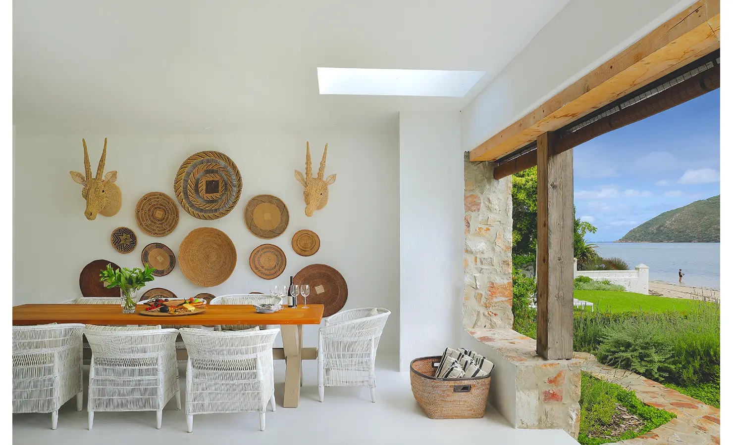 Perfect Hideaways: Light-filled dining space with white woven chairs and a basket wall, flowing out to the beach and lagoon, Knysna, Tides Reach