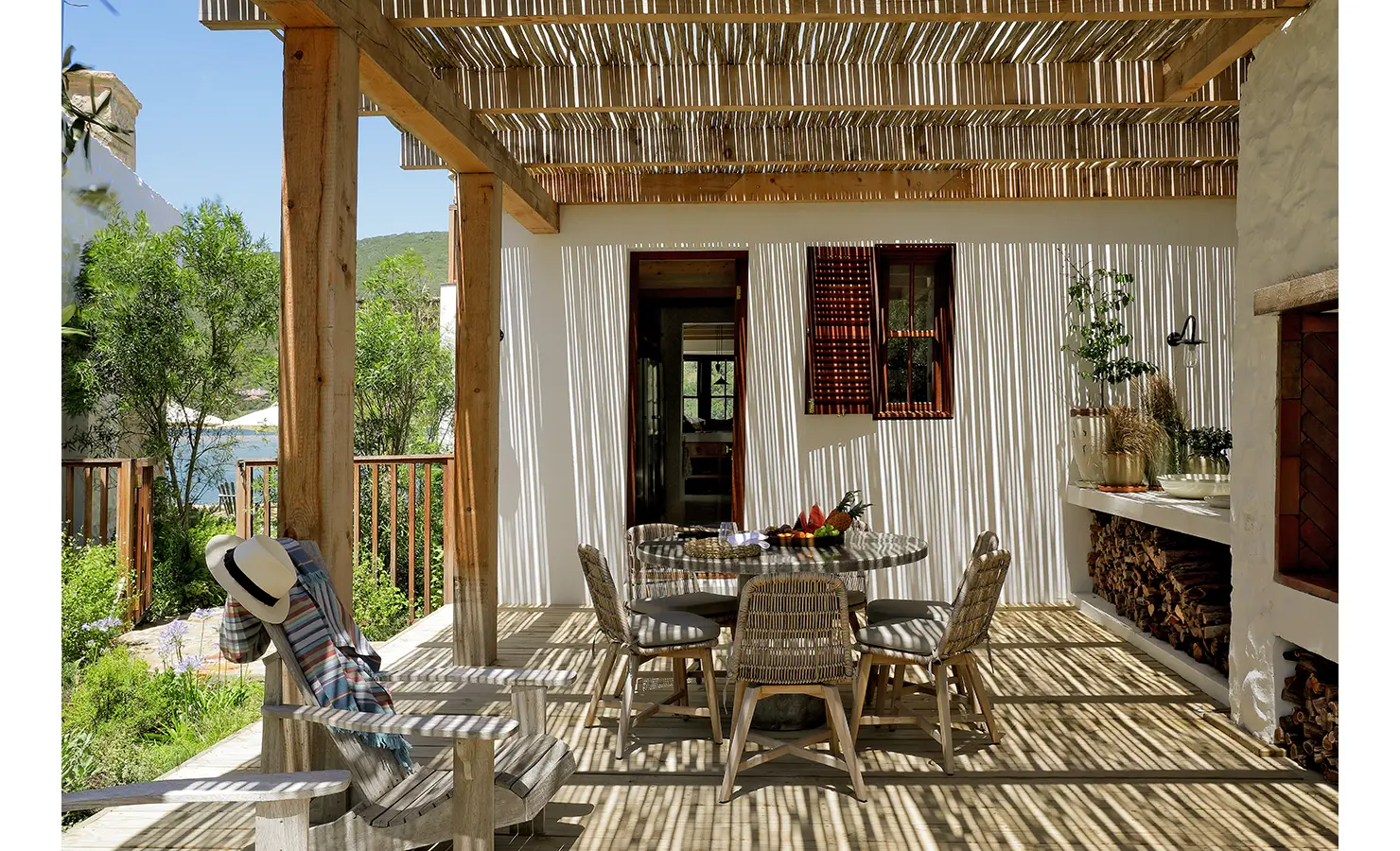 Perfect Hideaways: Pergola-shaded braai terrace with woven chairs, round table and outdoor prep counter stacked with firewood, Knysna, Tides Reach