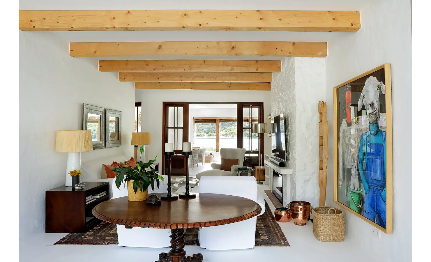 Perfect Hideaways: Art-filled living area with round wooden table, layered rugs and beams opening towards the water, Knysna, Tides Reach