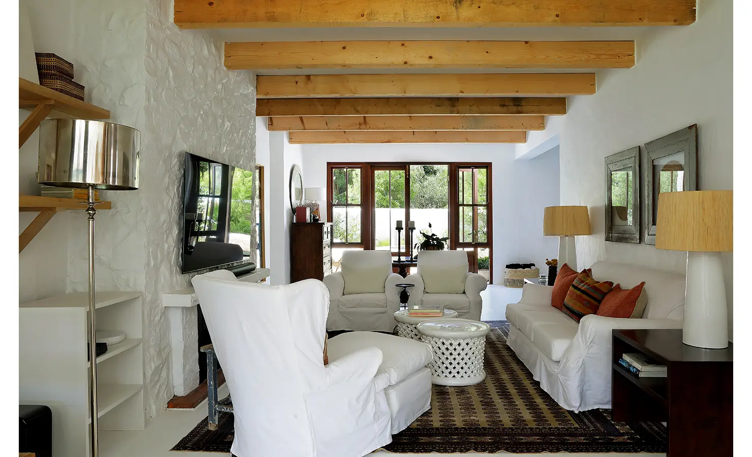 Perfect Hideaways: Cosy lounge with white slipcovered sofas and armchairs on a patterned rug, under timber beams and opening to garden views, Knysna, Tides Reach