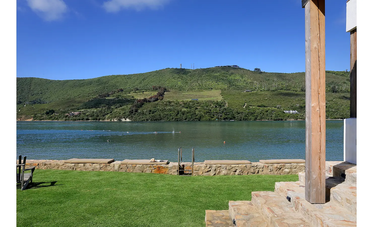 Perfect Hideaways: Lush lawn and stone steps down to the lagoon with built‑in sunbeds and a swim ladder, green hills beyond, Knysna, Tides Reach