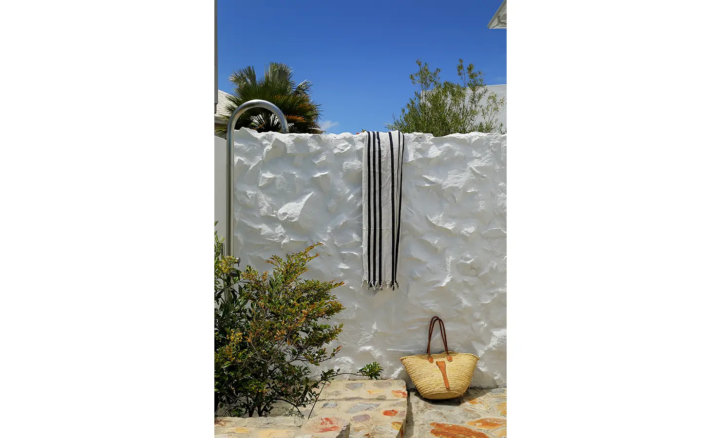 Perfect Hideaways: Outdoor shower against a textured white wall with striped towel and woven beach basket on stone paving, Knysna, Tides Reach