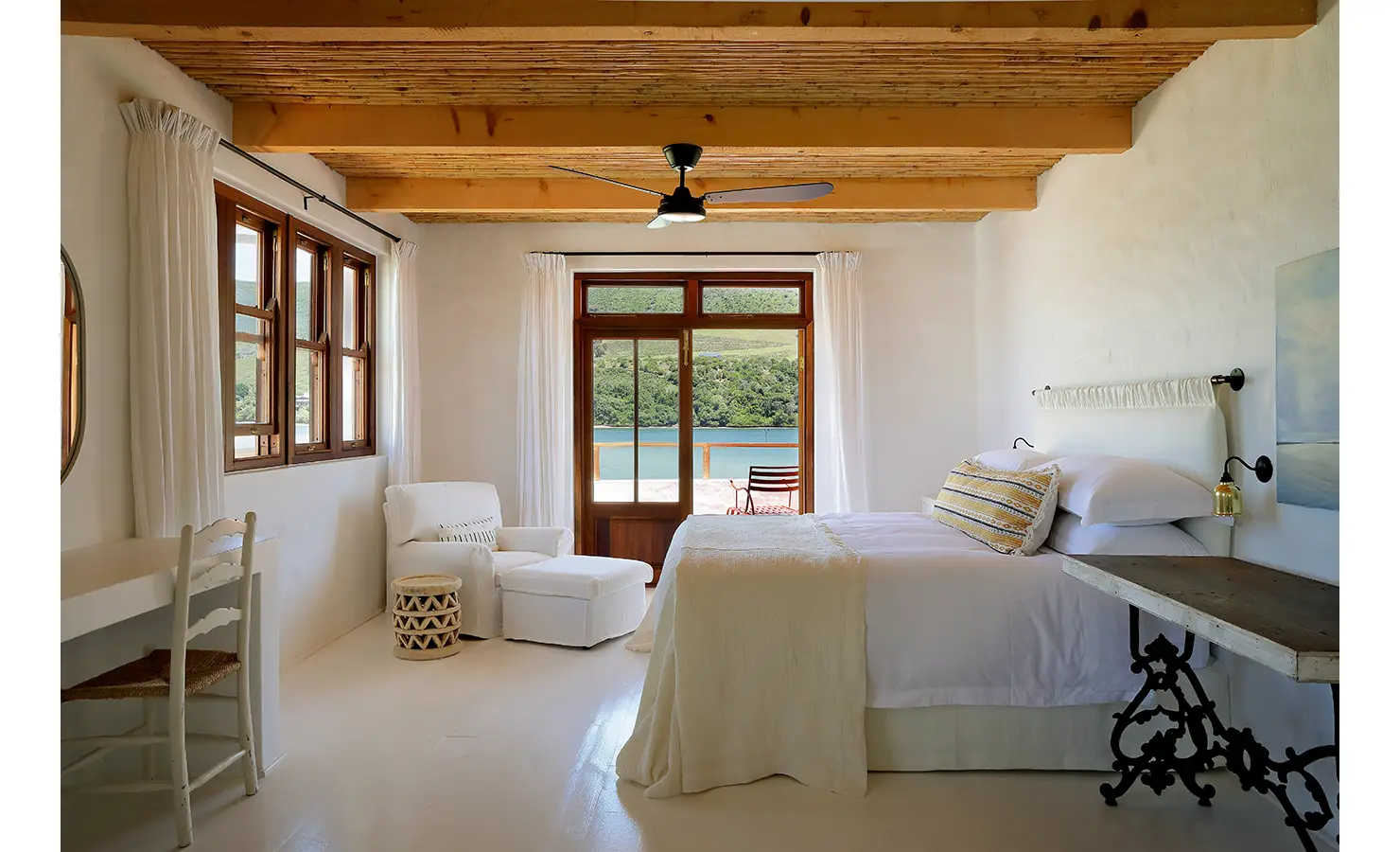 Perfect Hideaways: Calm bedroom in soft neutrals with rustic console desk, armchair and doors to a lagoon‑facing terrace, Knysna, Tides Reach