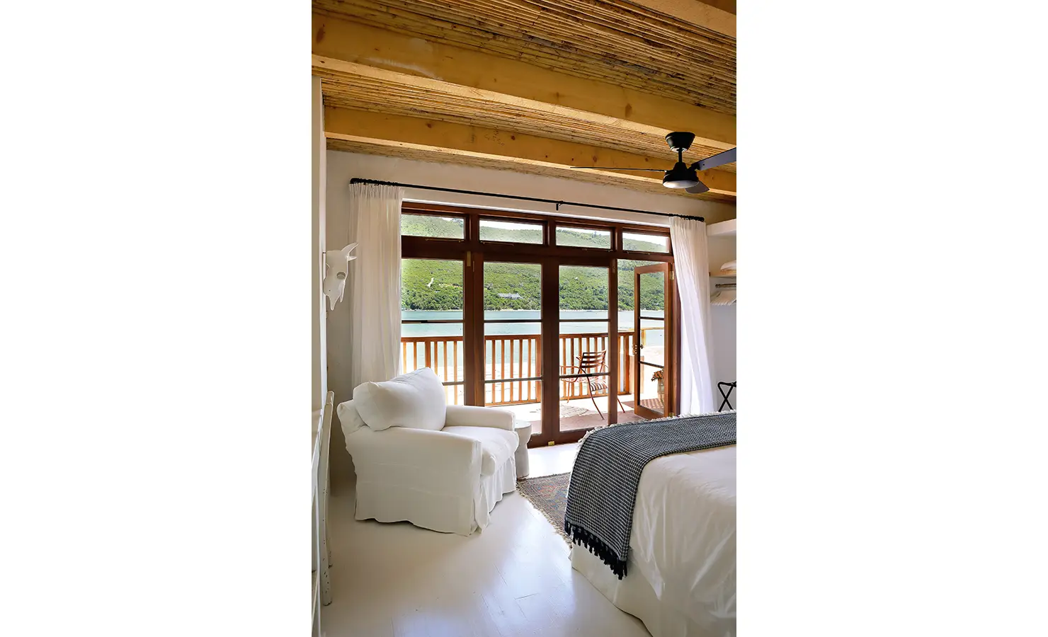 Perfect Hideaways: Light bedroom with reed-clad ceiling, white armchair and doors to a balcony above the lagoon, Knysna, Tides Reach