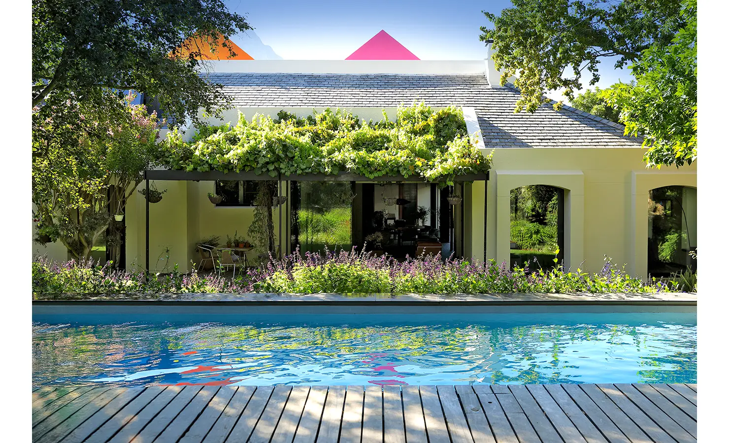 Perfect Hideaways: vine-draped verandah and pale-yellow façade reflected in a long lap pool with timber deck, framed by lush borders, Franschhoek, The Garden House