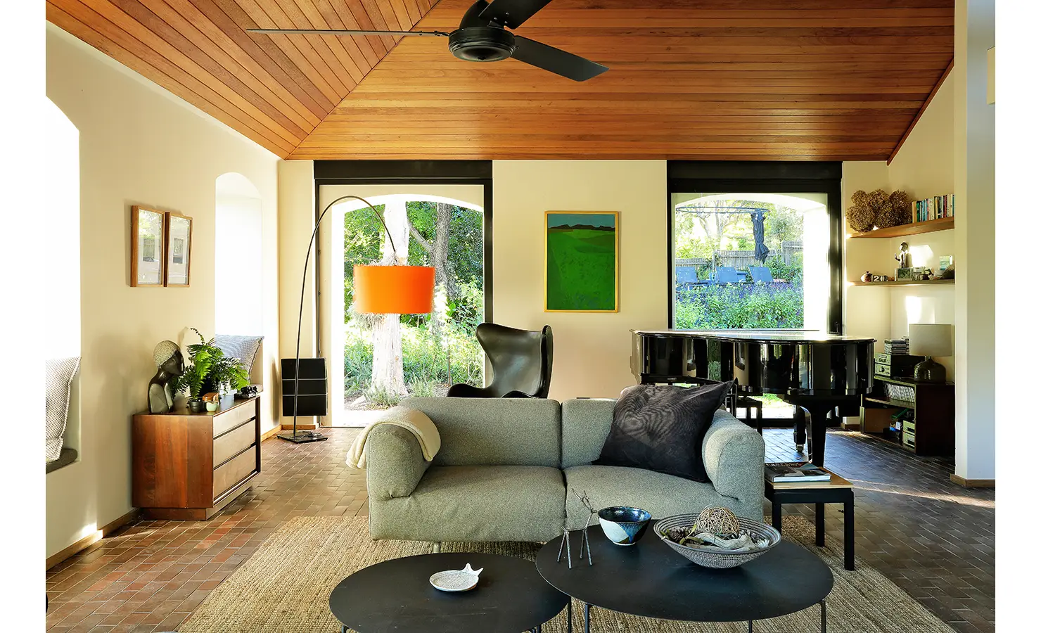 Perfect Hideaways: calm living room with timber ceiling, grey sofa, orange arc lamp and grand piano looking onto leafy gardens, Franschhoek, The Garden House