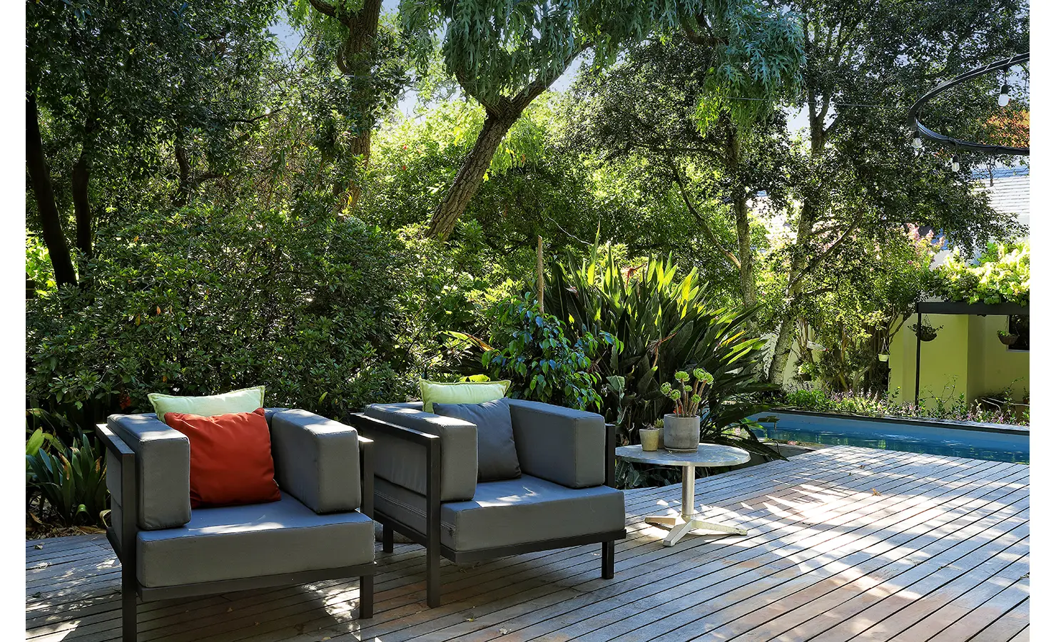 Perfect Hideaways: timber deck lounge with deep armchairs, colourful cushions and potted succulents beside the pool, surrounded by greenery, Franschhoek, The Garden House