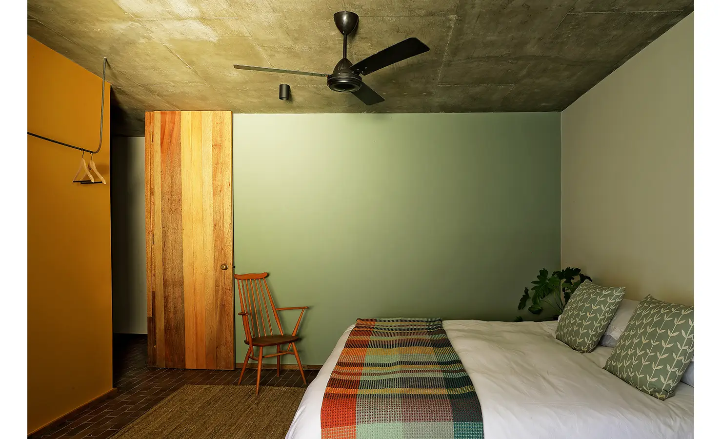 Perfect Hideaways: cosy bedroom with sage-green feature wall, concrete ceiling fan and patterned throw and cushions, Franschhoek, The Garden House