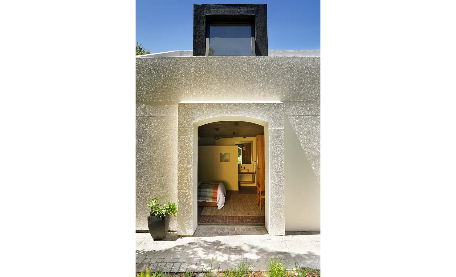 Perfect Hideaways: textured white façade with an arched entrance leading to the bedroom suite, black dormer above and a potted plant at the threshold, Franschhoek, The Garden House