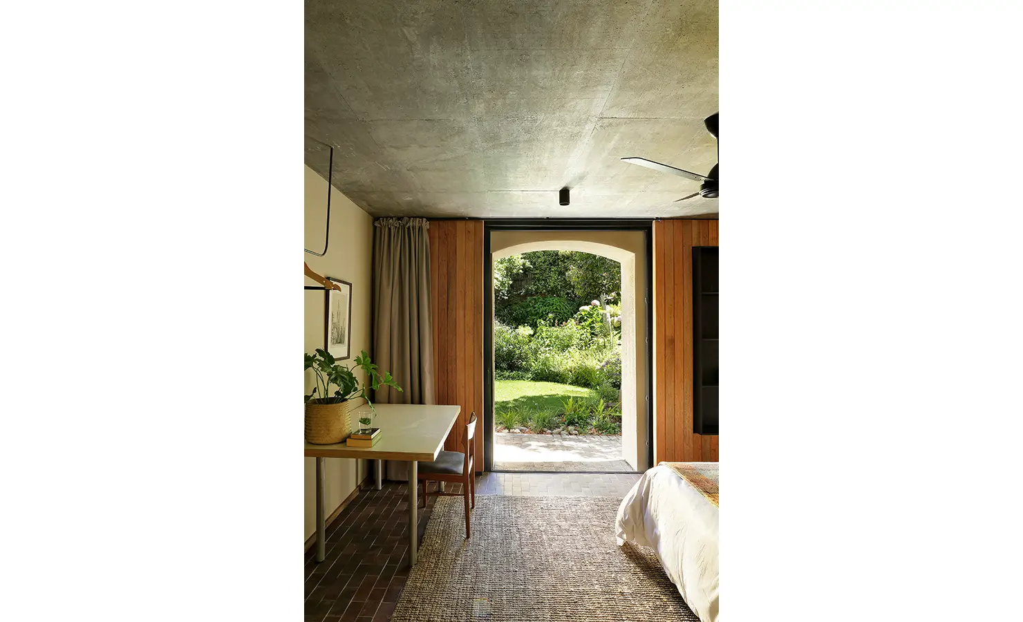 Perfect Hideaways: garden-facing bedroom with work desk and minimalist hanging rail, arched doorway framing lush greenery, Franschhoek, The Garden House