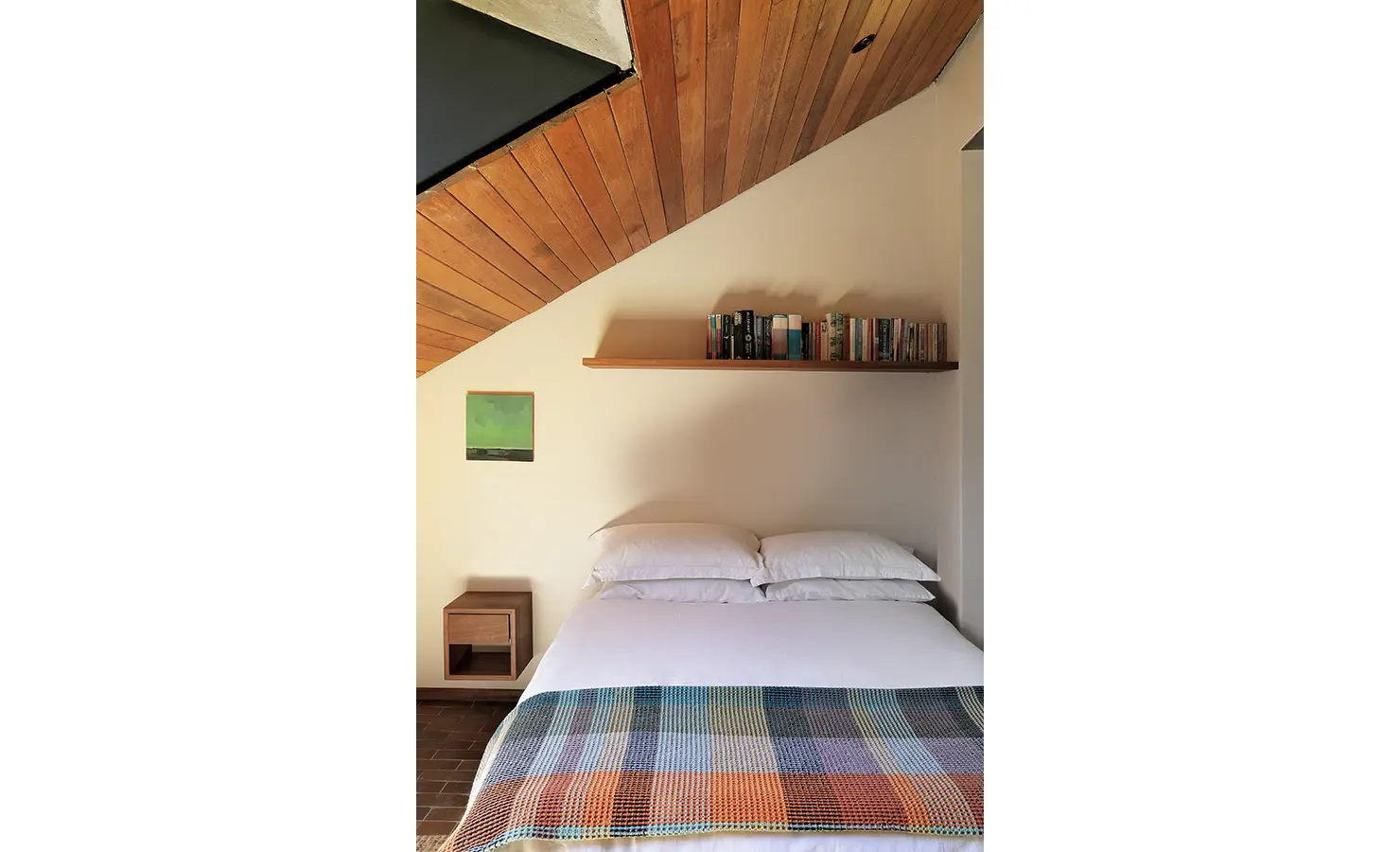 Perfect Hideaways: simple bedroom with slanted timber ceiling, shelf of books and a plaid throw over crisp white bedding, Franschhoek, The Garden House