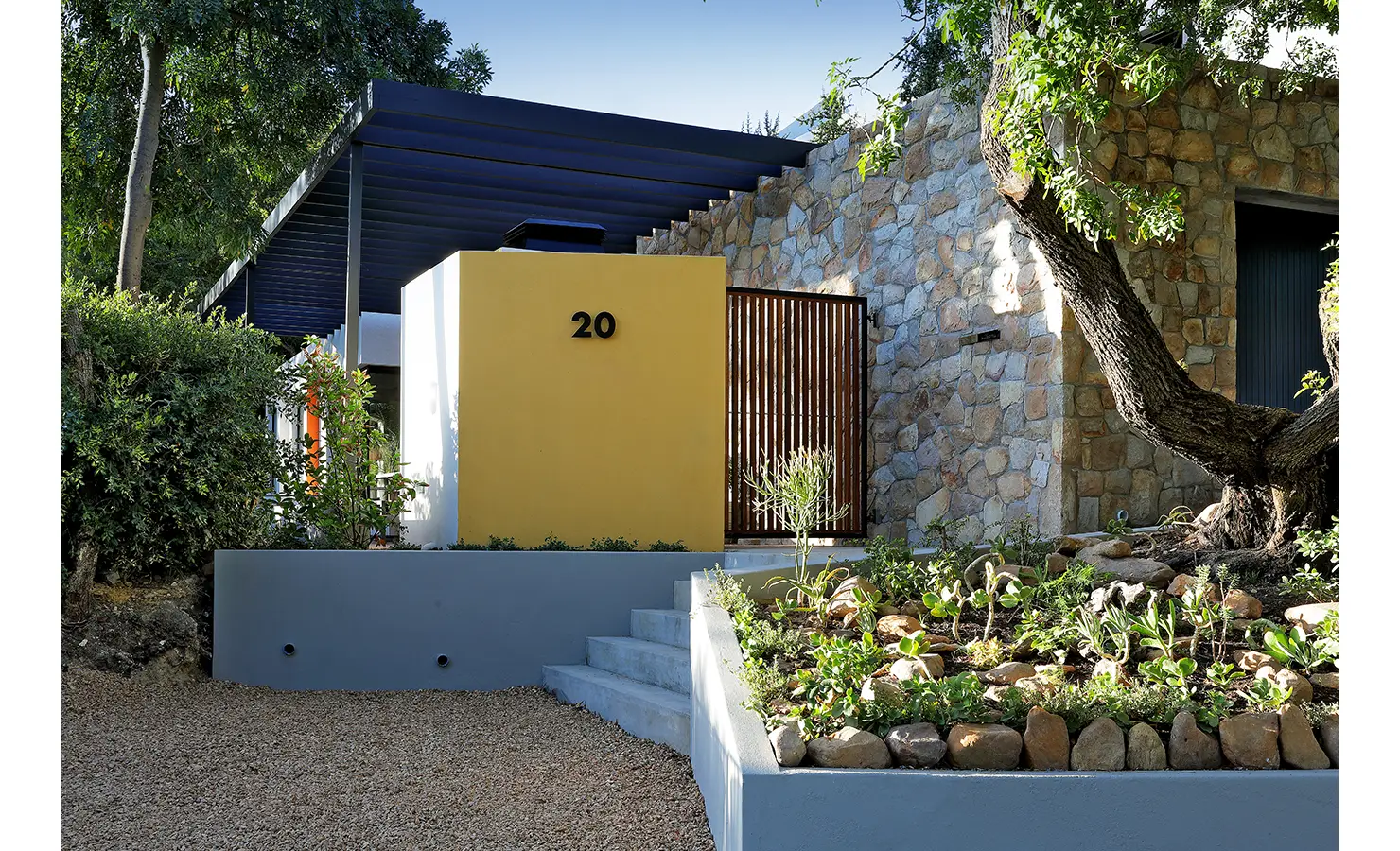 Perfect Hideaways: contemporary entrance with mustard cube, number 20, stone feature wall and gravelled garden with succulents beneath a slatted pergola, Franschhoek, The Garden House