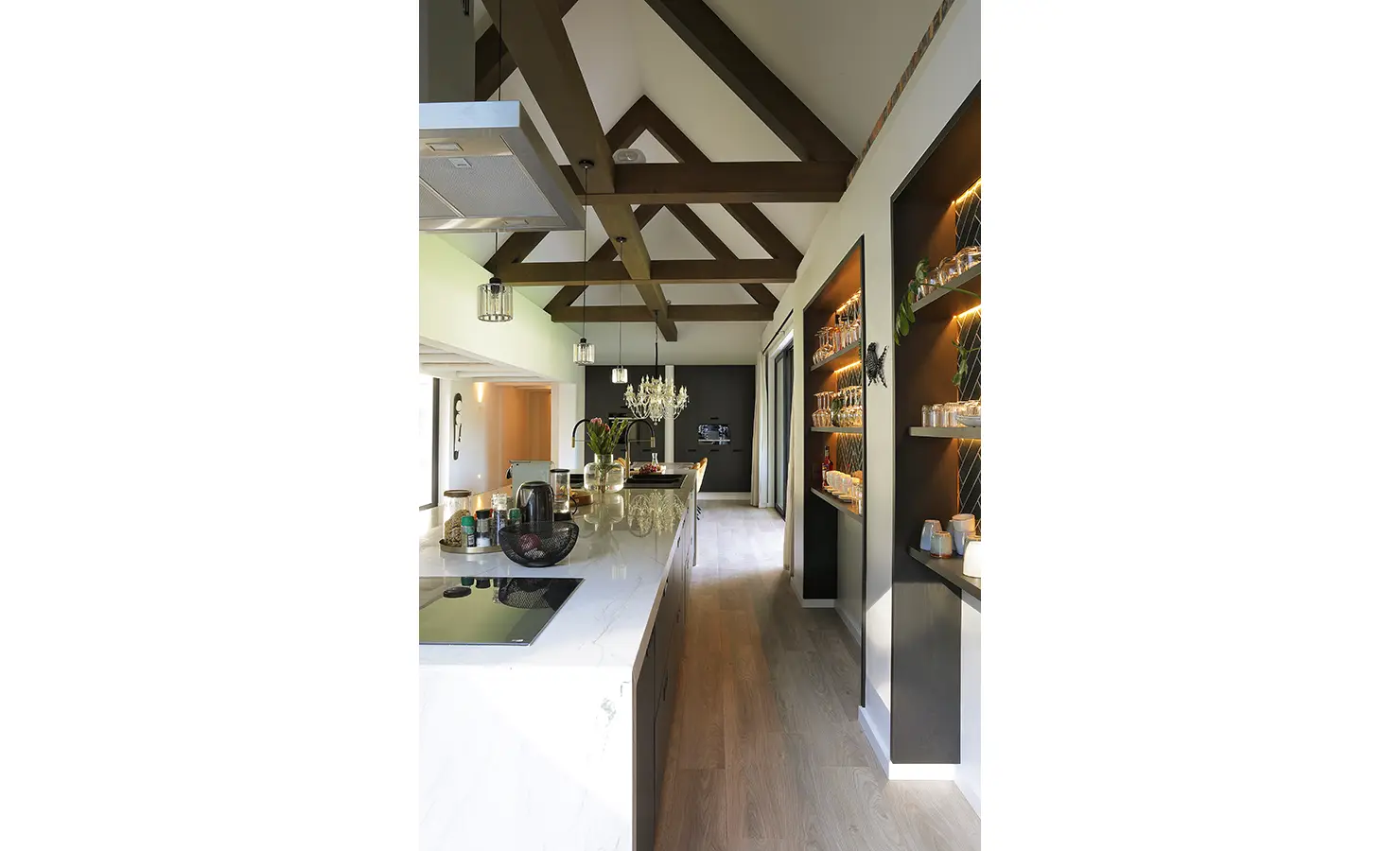 Perfect Hideaways: A sleek modern kitchen with a marble island, ambient pendant lighting, open display shelving, and exposed wooden trusses overhead, exuding sophistication and warmth. Bel Ombre Hills, Constantia.