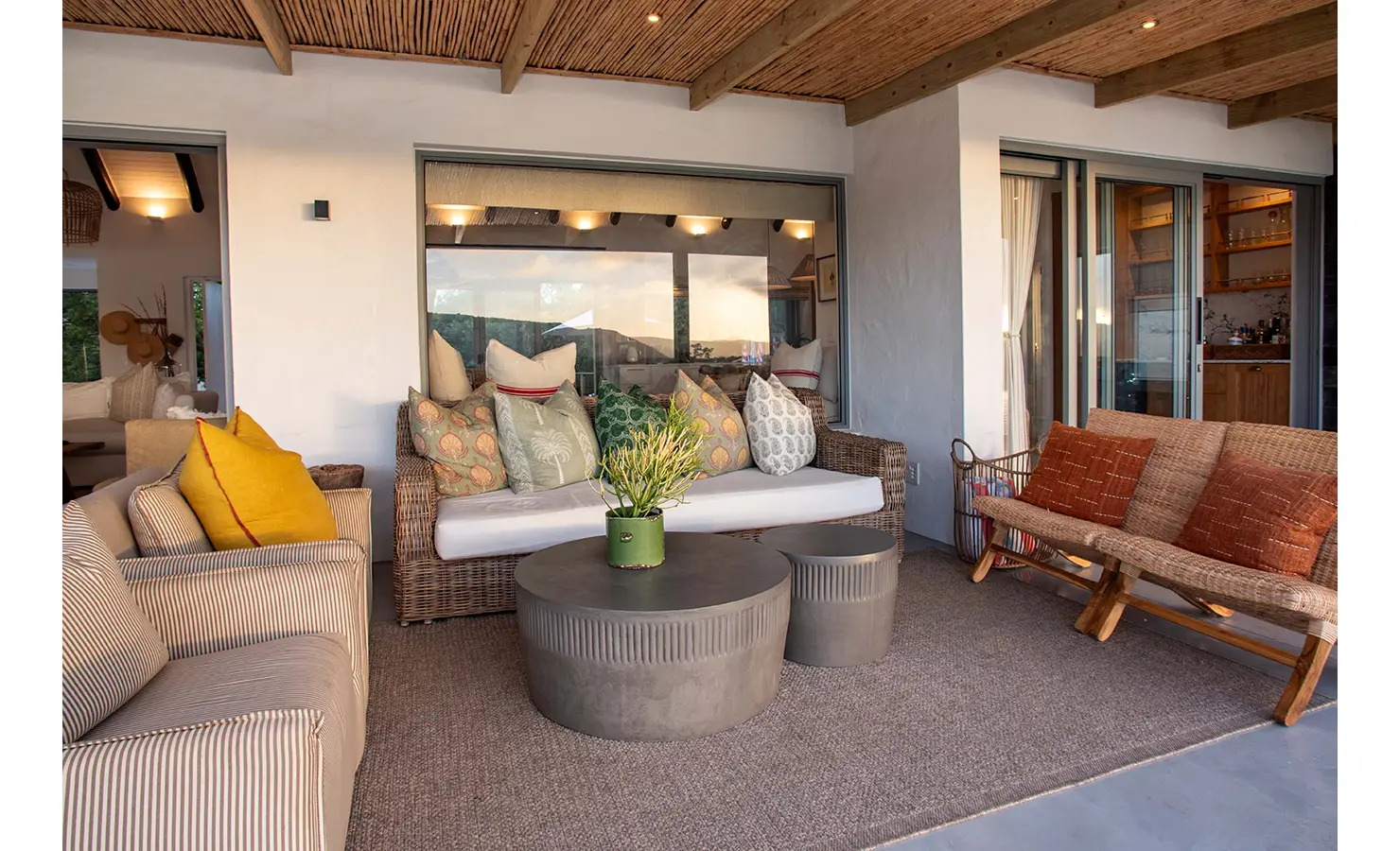 Perfect Hideaways: A charming outdoor seating nook beneath a bamboo-covered patio is styled with patterned scatter cushions and a contemporary stone table, reflecting relaxed riverside living. River Run, Plettenberg Bay.