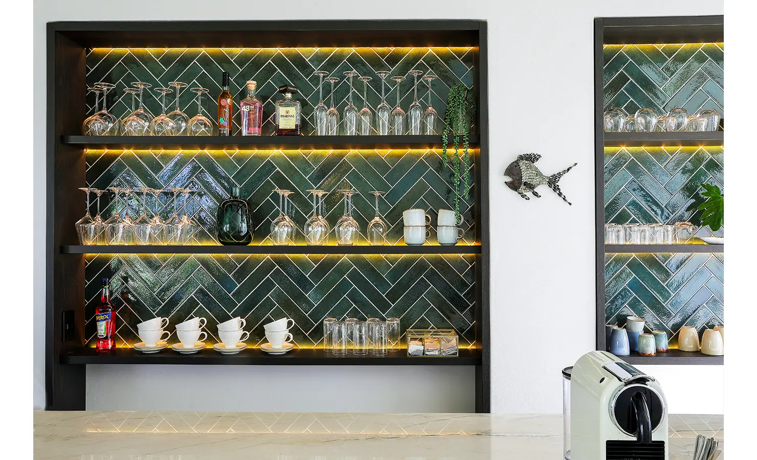 Perfect Hideaways: A close-up of stylish open shelves with green herringbone tiles, accent lighting, and neatly arranged glassware and ceramics, adding a bold yet refined design statement. Bel Ombre Hills, Constantia.