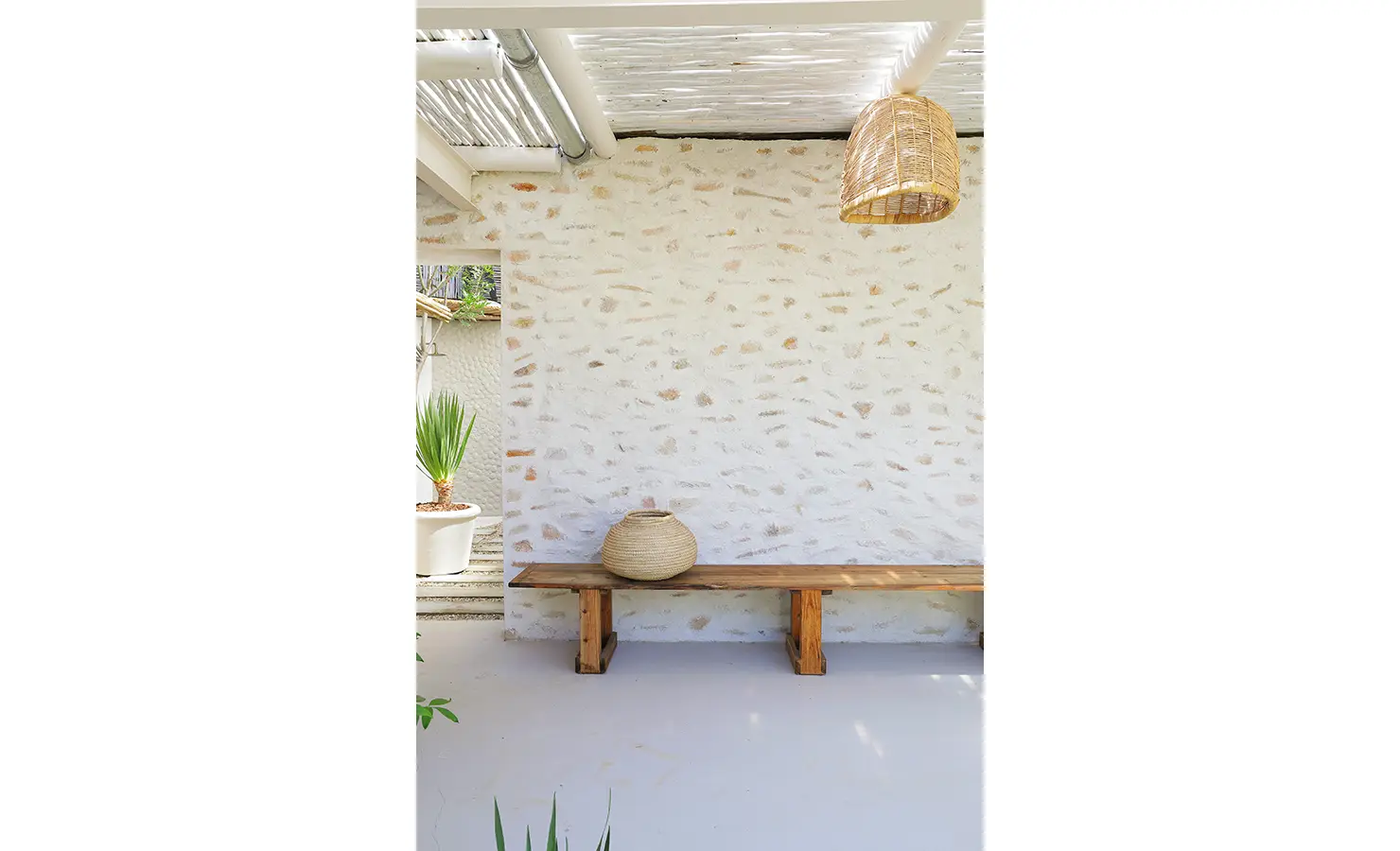 Perfect Hideaways: A rustic outdoor bench sits beneath a woven rattan light, against a textured stone wall, creating a simple and tranquil corner beneath a pergola. Bel Ombre Hills, Constantia.
