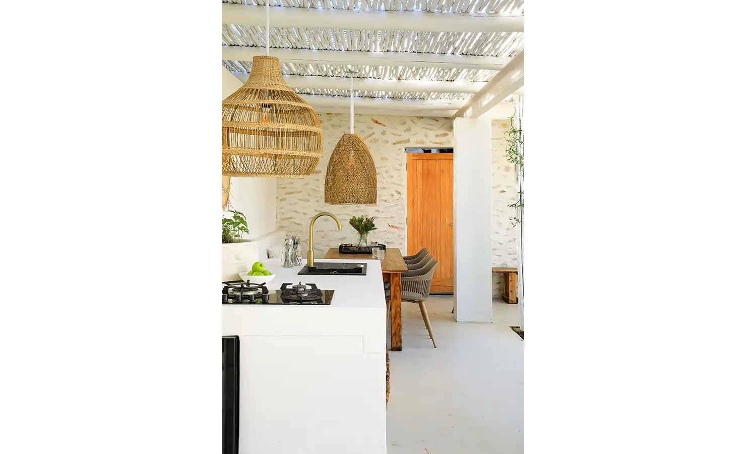 Perfect Hideaways: An inviting outdoor kitchen and dining space with natural textures, rattan lighting, a pale palette, and warm timber accents. Bel Ombre Hills, Constantia.