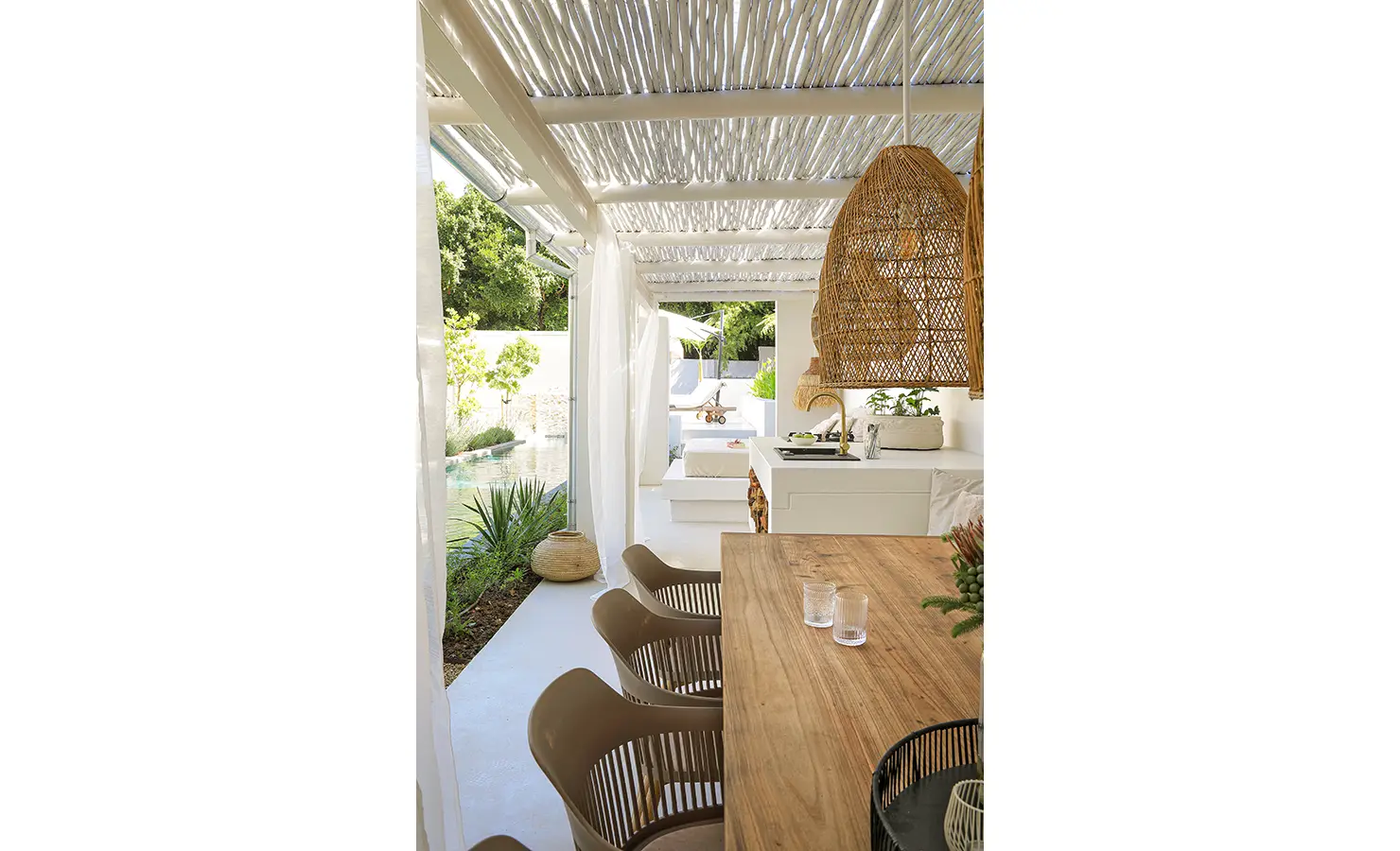 Perfect Hideaways: A tranquil poolside dining area with a timber table, contemporary chairs, and sheer curtains flowing in the breeze beneath a woven ceiling. Bel Ombre Hills, Constantia.