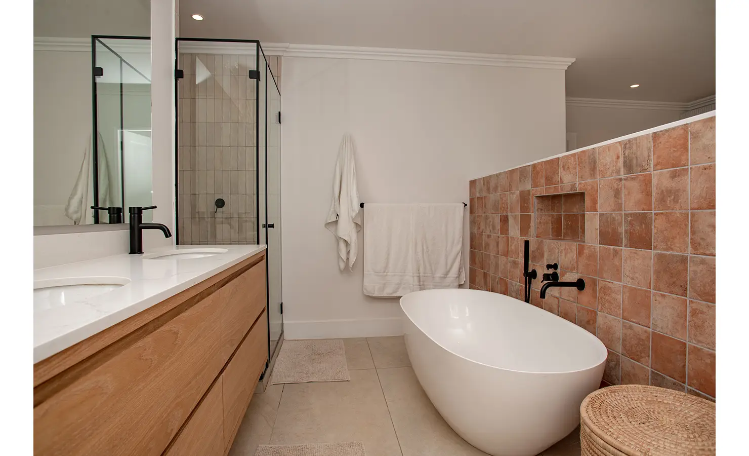 Perfect Hideaways: A spa-like bathroom features a freestanding oval bath, terracotta tiling, a walk-in shower, and a sleek wood vanity with dual basins. River Run, Plettenberg Bay.