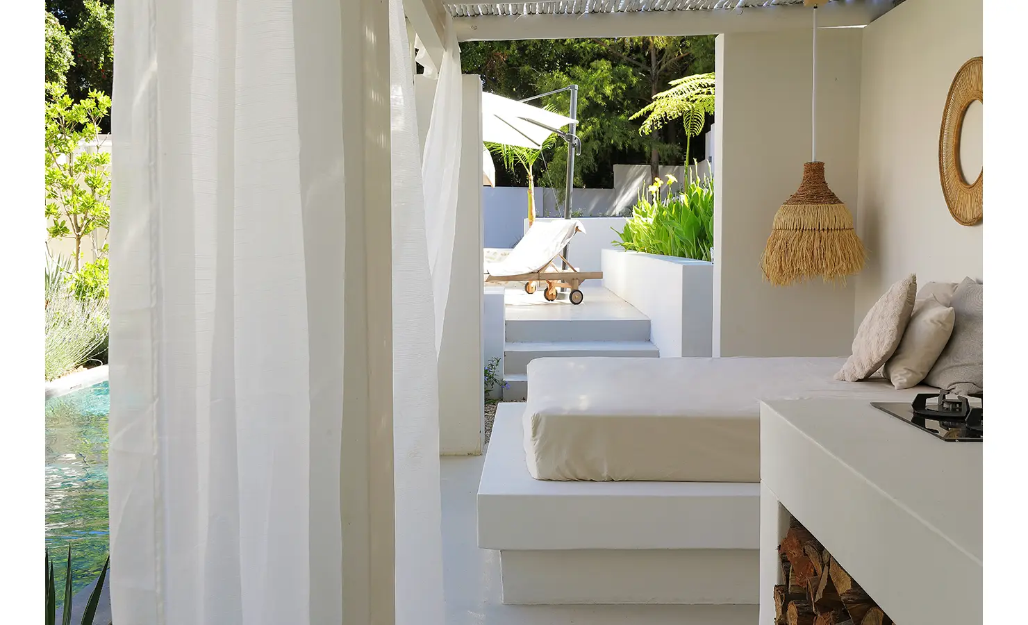 Perfect Hideaways: A peaceful shaded terrace with a daybed, flowing white curtains, and a straw pendant light, overlooking the pool and sun loungers. Bel Ombre Hills, Constantia.