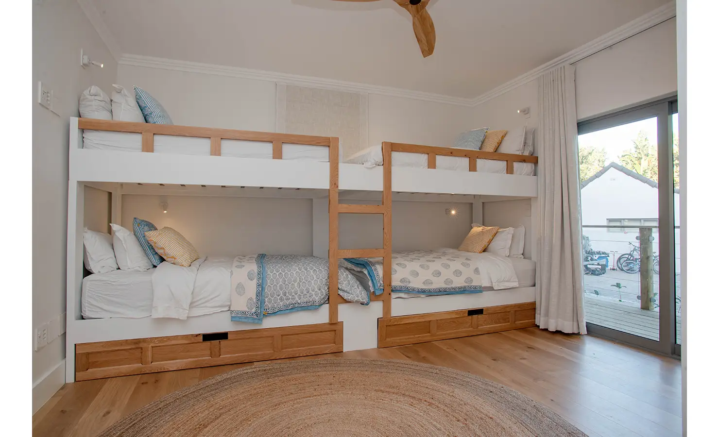 Perfect Hideaways: A light-filled children's room features two sets of bunk beds with playful blue and yellow bedding, natural wood finishes, and sliding doors opening to the garden. River Run, Plettenberg Bay.