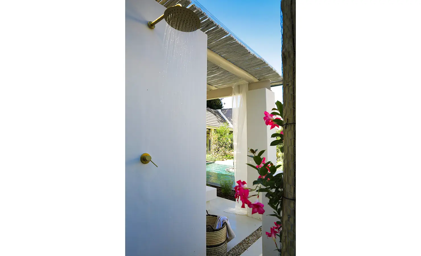 Perfect Hideaways: An outdoor brass rain shower stands against a white privacy wall, framed by flowering vines and overlooking the serene pool area. Bel Ombre Hills, Constantia.