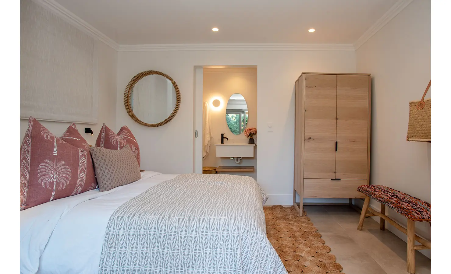 Perfect Hideaways: This inviting bedroom pairs rustic woven textures with soft pinks and a view into the en-suite bathroom, creating a warm, welcoming atmosphere. River Run, Plettenberg Bay.